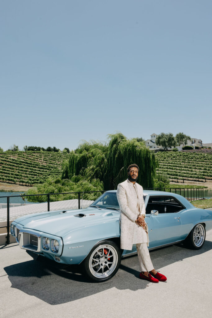 Black Groom posed in front of vintage blue car at Lavanda at Leal Vineyards