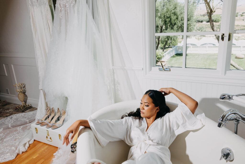 Black bride sitting in a clawfoot bathtub in her wedding pajamas, styled as a high-fashion vogue editorial portrait with dramatic lighting.