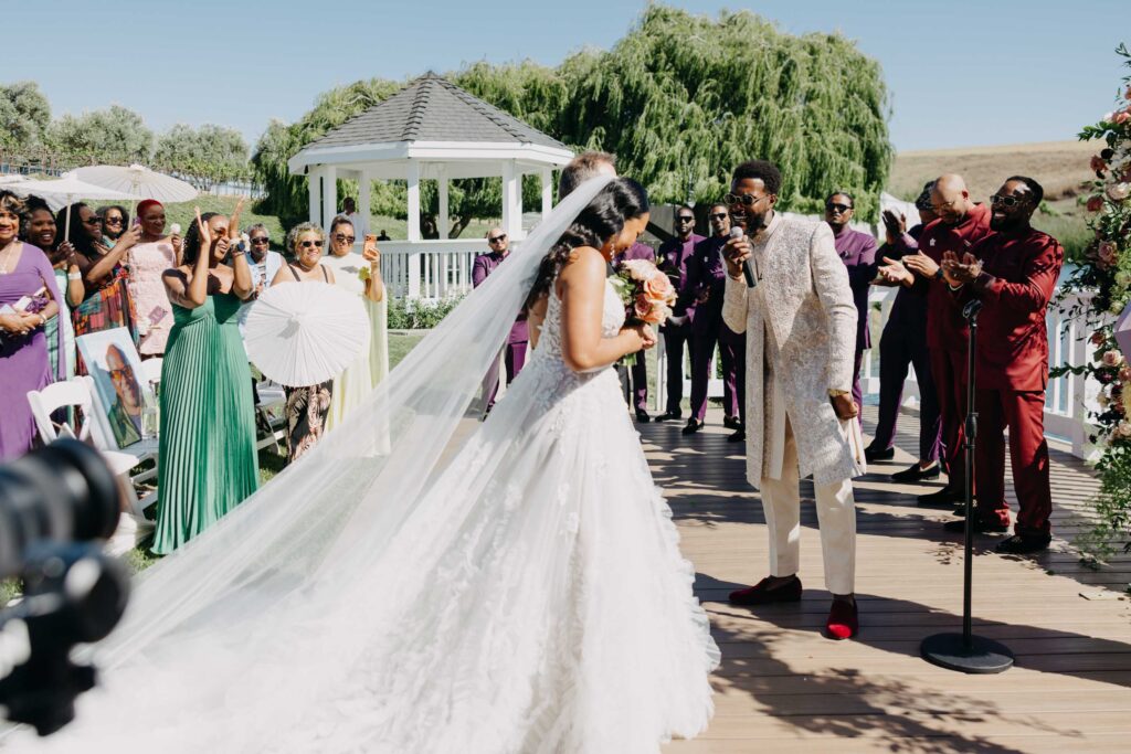 Black bride walking down the aisle at an outdoor vineyard wedding ceremony, guests standing on either side.