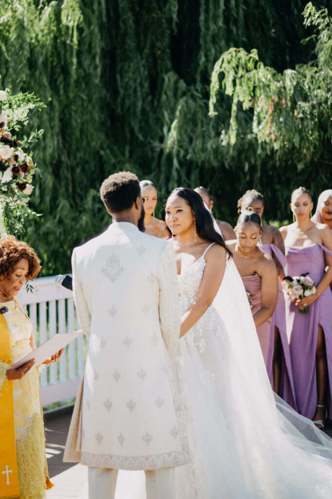 Black bride and groom exchanging vows under a floral arch at Lavanda Leal Vineyards, rows of grapevines in the background.