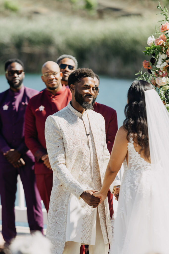Black bride and groom exchanging vows under a floral arch at Lavanda Leal Vineyards, rows of grapevines in the background.