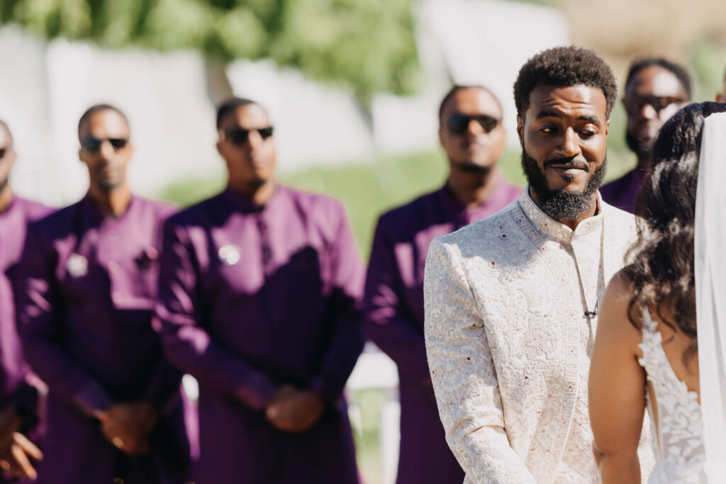 Black bride and groom exchanging vows under a floral arch at Lavanda Leal Vineyards, rows of grapevines in the background.