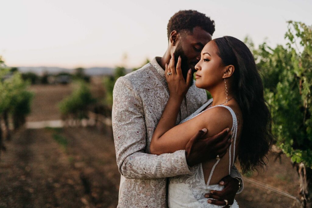 Black bride and groom in a dramatic, high-contrast portrait among the vineyard rows at sunset.