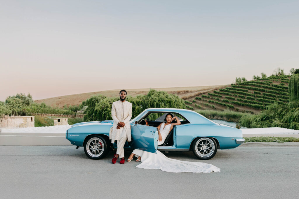 Black bride and groom posed in front of vintage blue car at golden hour at Lavanda Leal Vineyards.