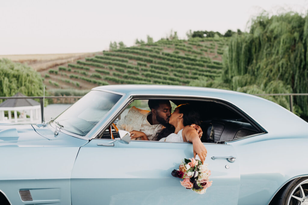 Black bride and groom posed in front of vintage blue car at golden hour at Lavanda Leal Vineyards.