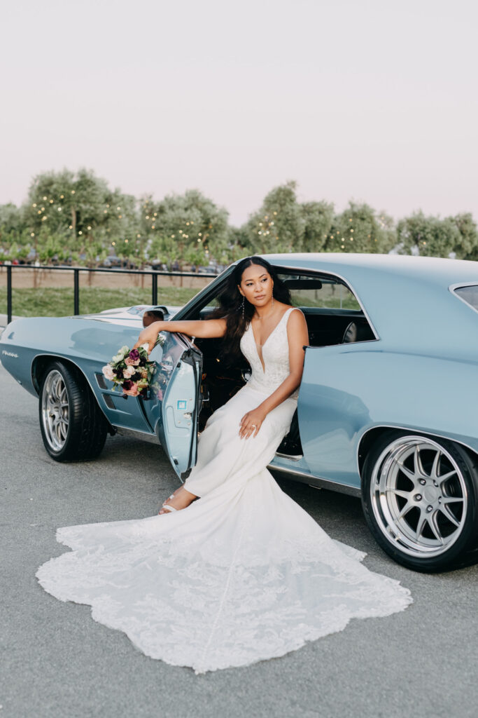 Black bride posed in front of vintage blue car at golden hour at Lavanda Leal Vineyards.