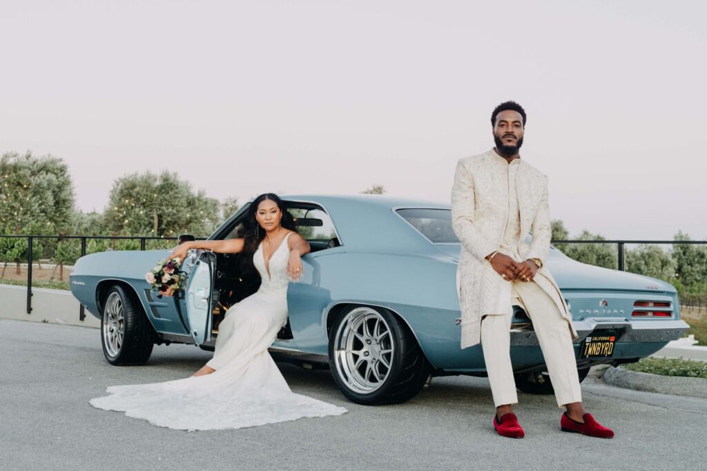 Black bride and groom posed in front of vintage blue car at golden hour at Lavanda Leal Vineyards.